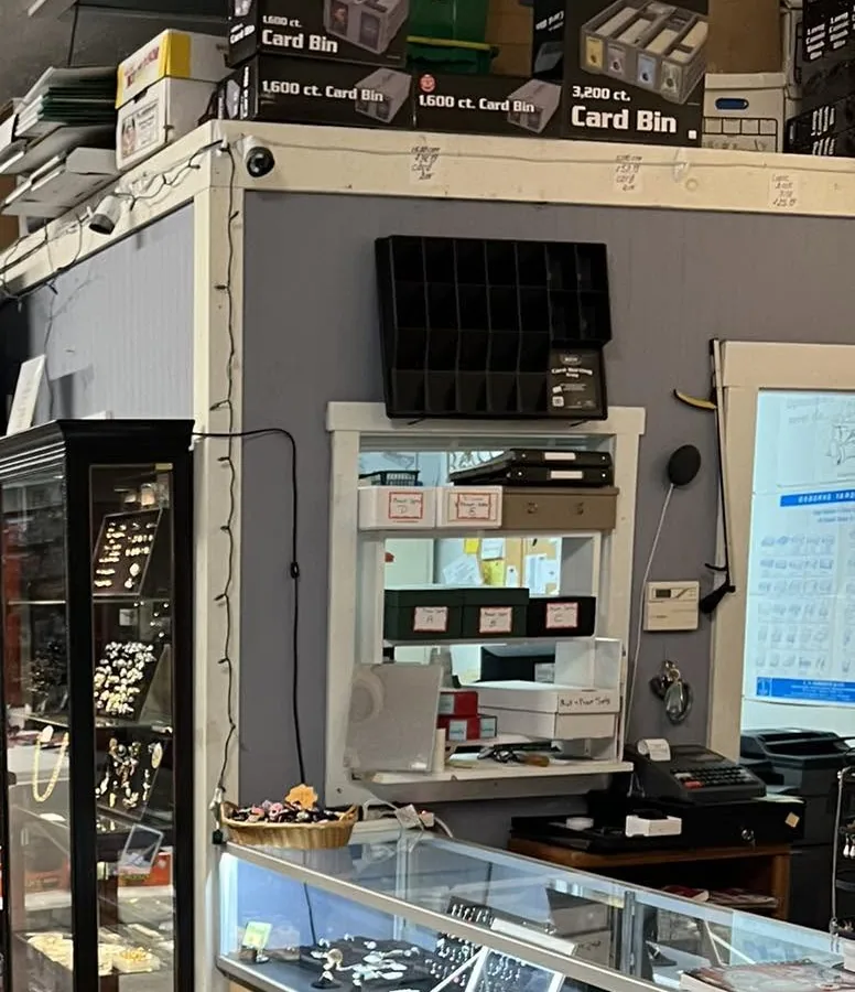 Glass display cases of coins and jewelry inside Roc Collectibles, with boxes of card bins stacked above